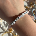 Little Words Project Bracelet with 'FRESH START' on a wrist against a glittery background