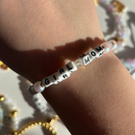 Little Words Project Bracelet with 'GIRL MOM' beads on a wrist against a blurred background