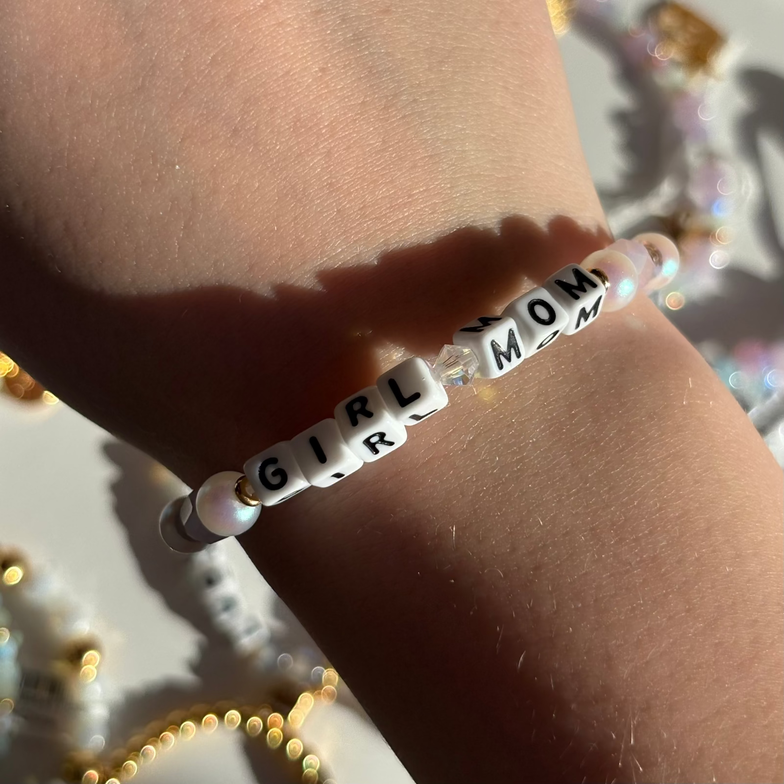 Little Words Project Bracelet with 'GIRL MOM' beads on a wrist against a blurred background