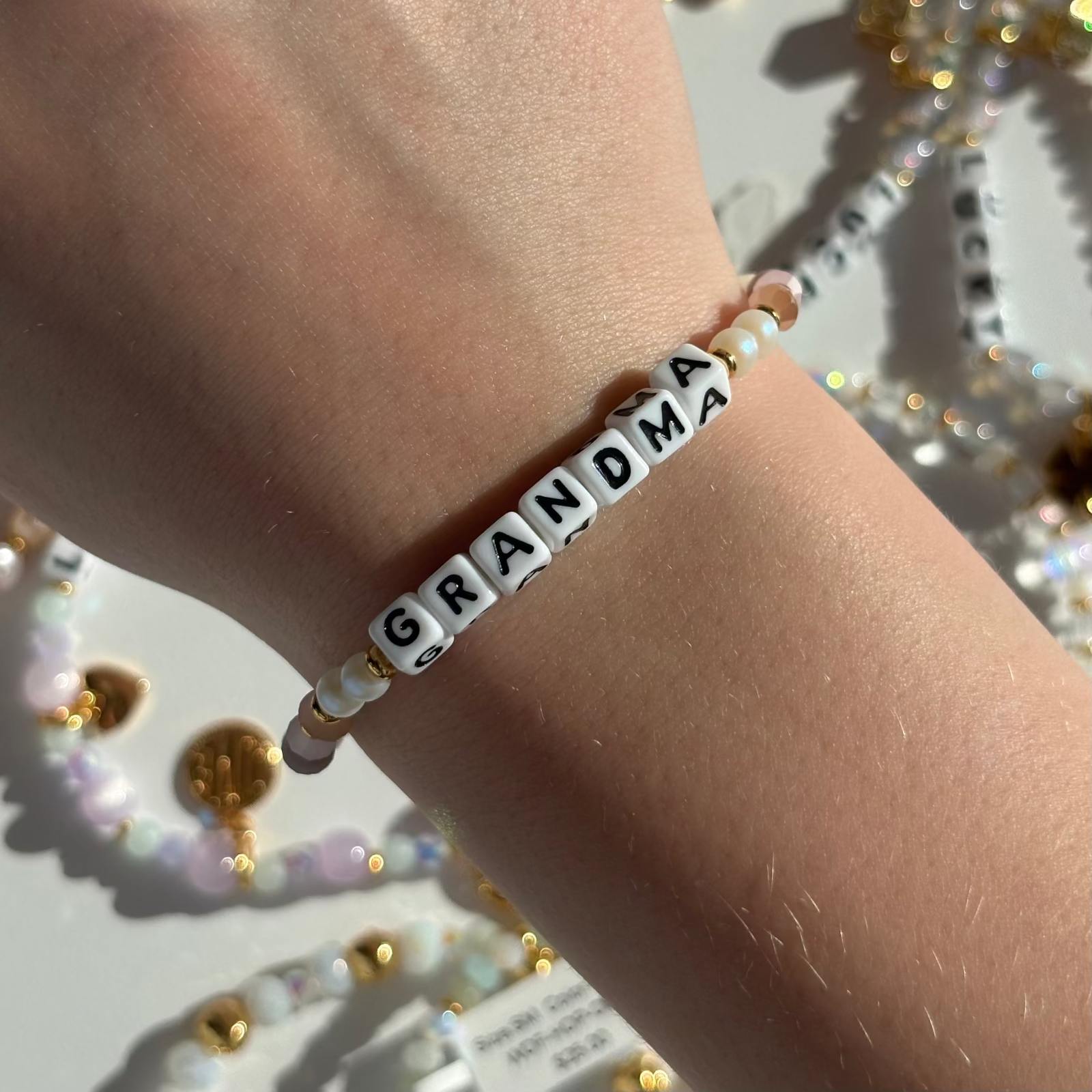 Little Words Project Bracelet with 'GRANDMA' beads on a wrist, with decorative beads in the background.