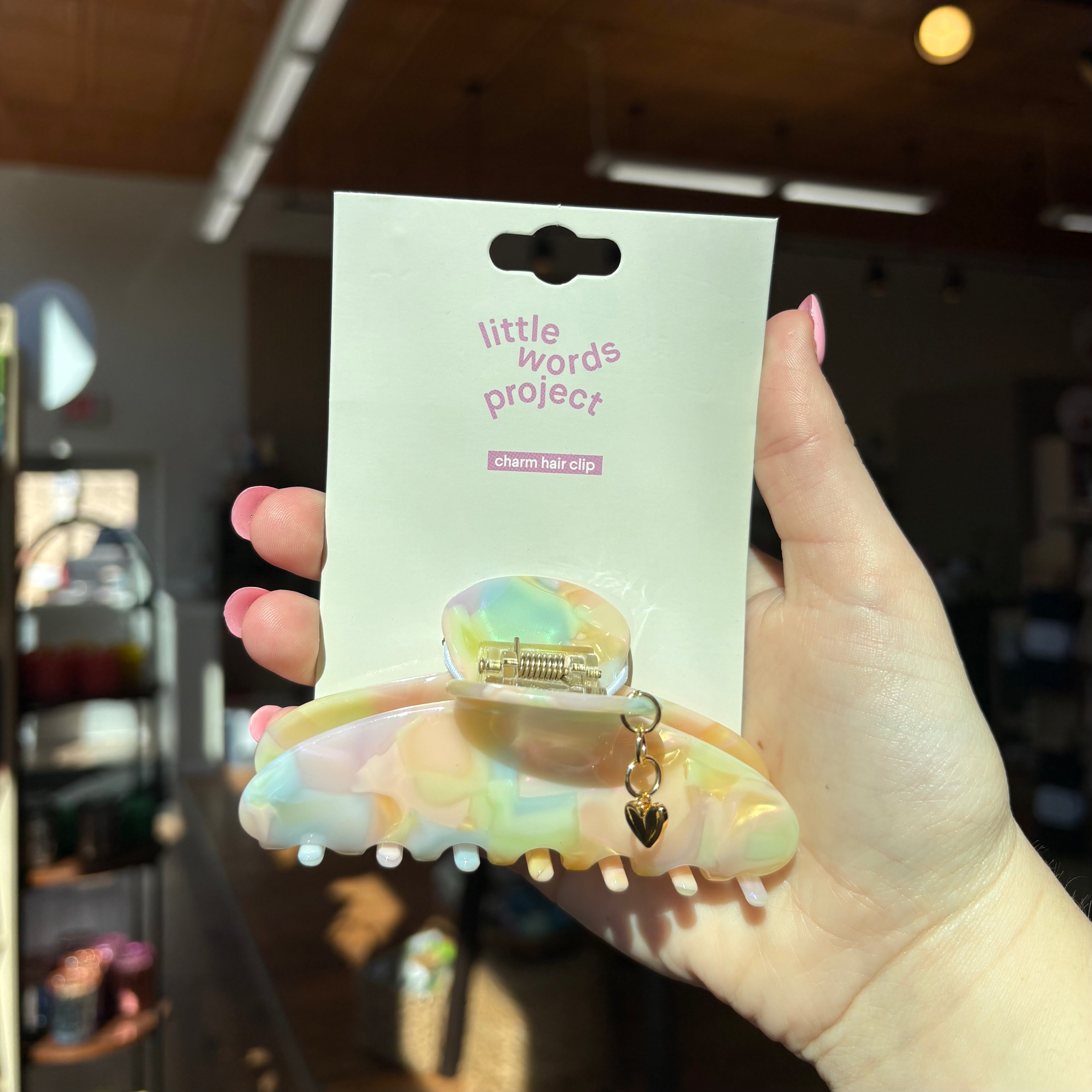 Hand holding a 'little words project' puffy heart charm hair clip with packaging
