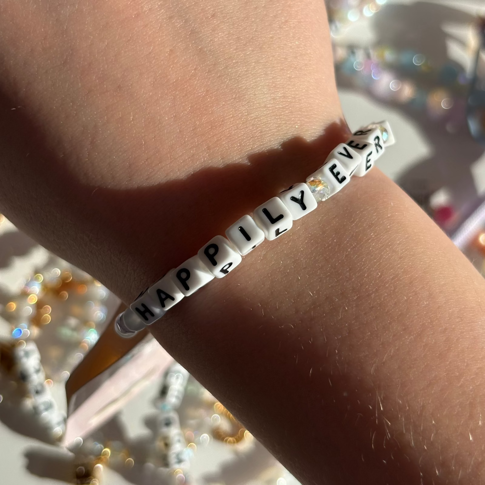 Little Words Project Bracelet with 'HAPPILY EVER' on a wrist with a blurred jewelry background