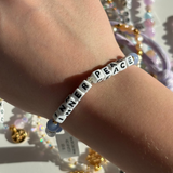Little Words Project Bracelet with 'Inner Peace' letter beads on a wrist, with a blurred background of jewelry.