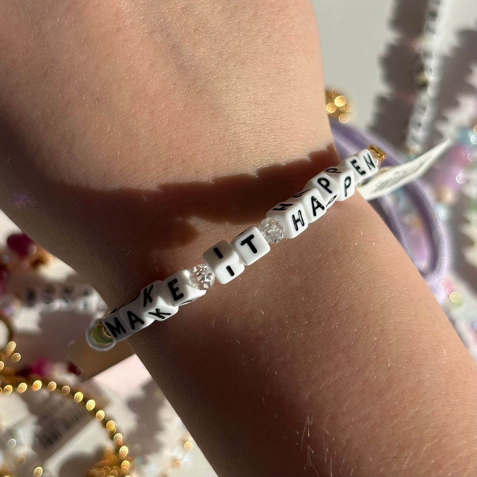 Little Words Project Bracelet with 'MAKE IT HAPPEN' message on wrist with colorful background