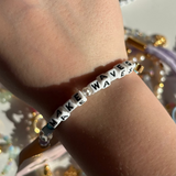Little Words Project Bracelet with 'MAKE WAVES' beads on a wrist against a glittery background
