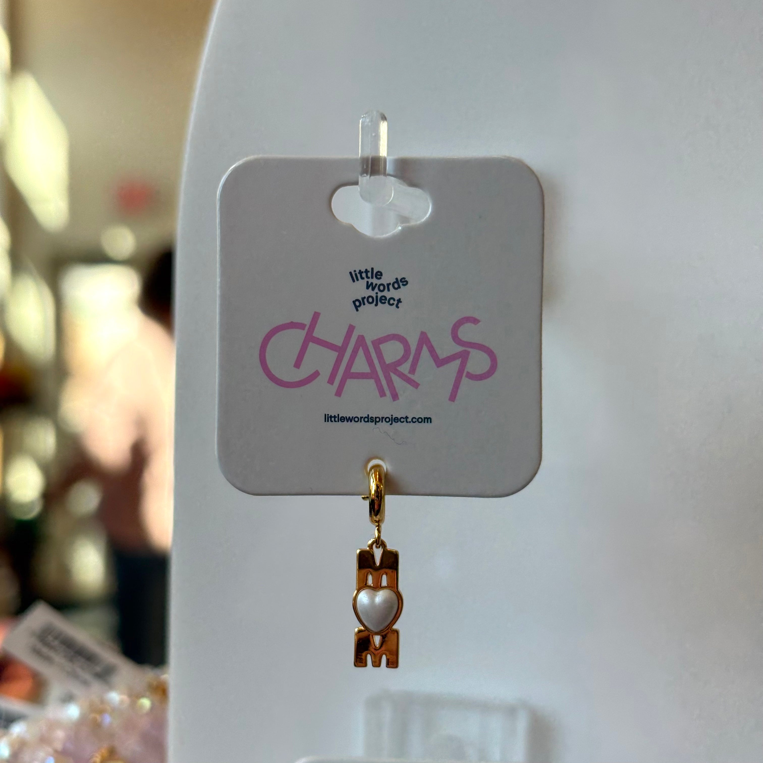 Gold mom charm on a 'little words project' card with blurred background