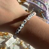 Bracelet with 'Moon & Back' text on a wrist, with blurred jewelry store background.