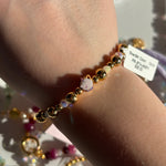 Gold beaded disney "mrs potts" bracelet on a wrist with a visible tag, against a neutral background.