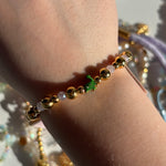 Gold beaded pascal disney bracelet with a green charm on a wrist against a blurred background