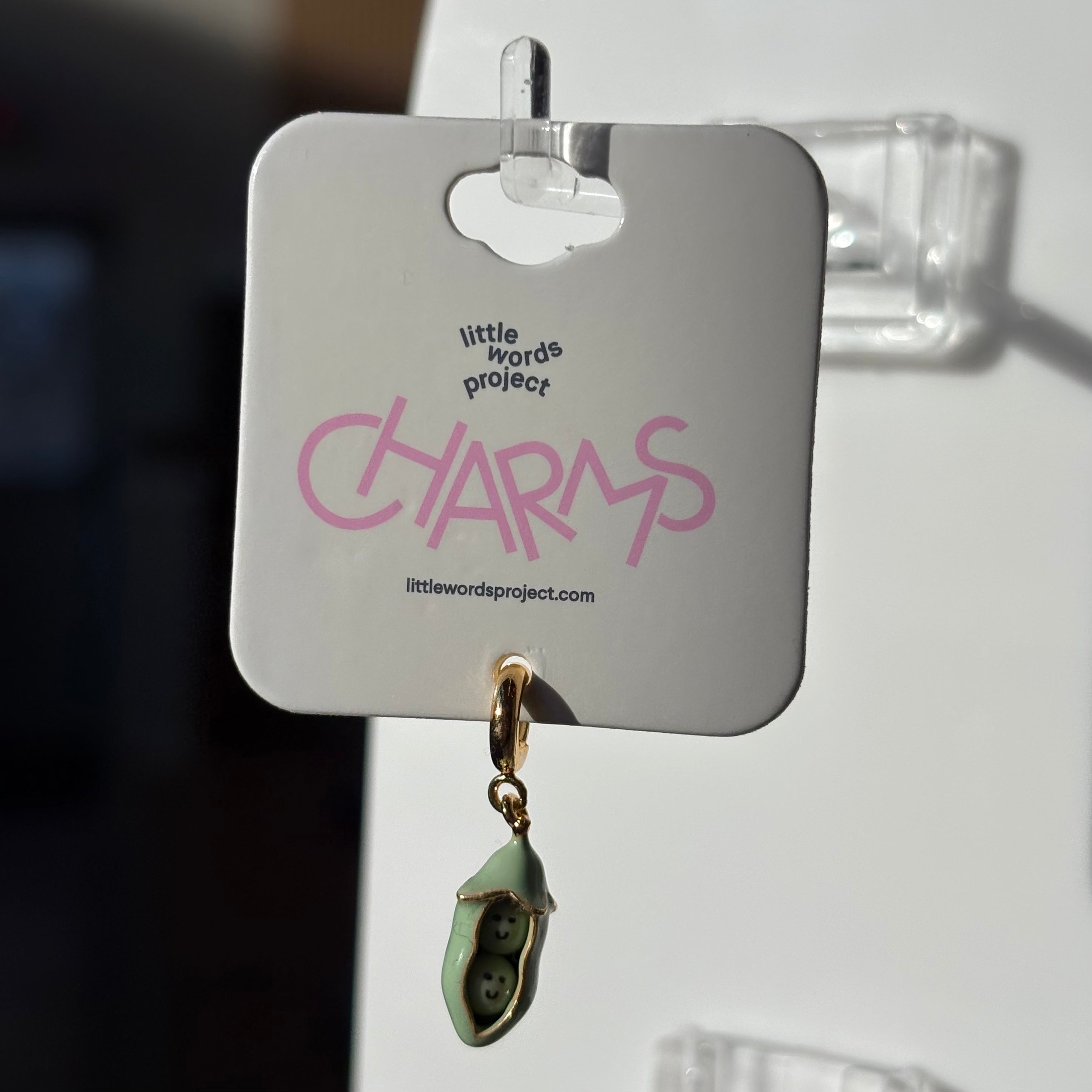 Green two peas charm on a 'Little Words Project' card with a blurred background