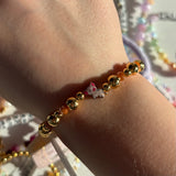 Gold beaded bracelet with a small pig named pua from moana disney charm on a wrist, with a blurred colorful background.