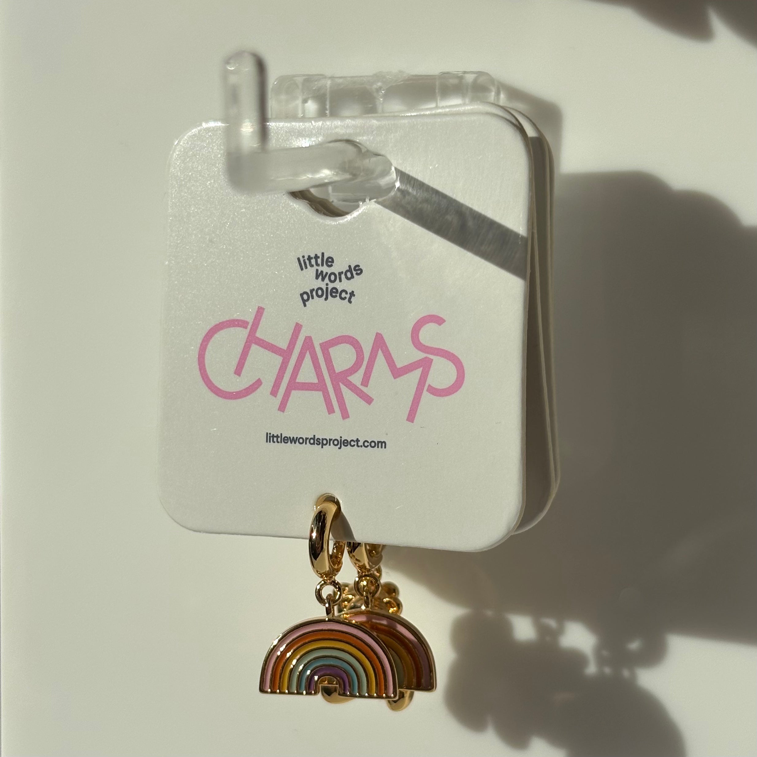 Rainbow charm on a card with 'little words project' branding