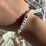 Little Words Bracelet with 'RENEW' beads on a wrist, with a blurred background of jewelry.