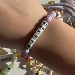 Little Words Project Bracelet with 'SISTER' beads on a wrist, with jewelry in the background