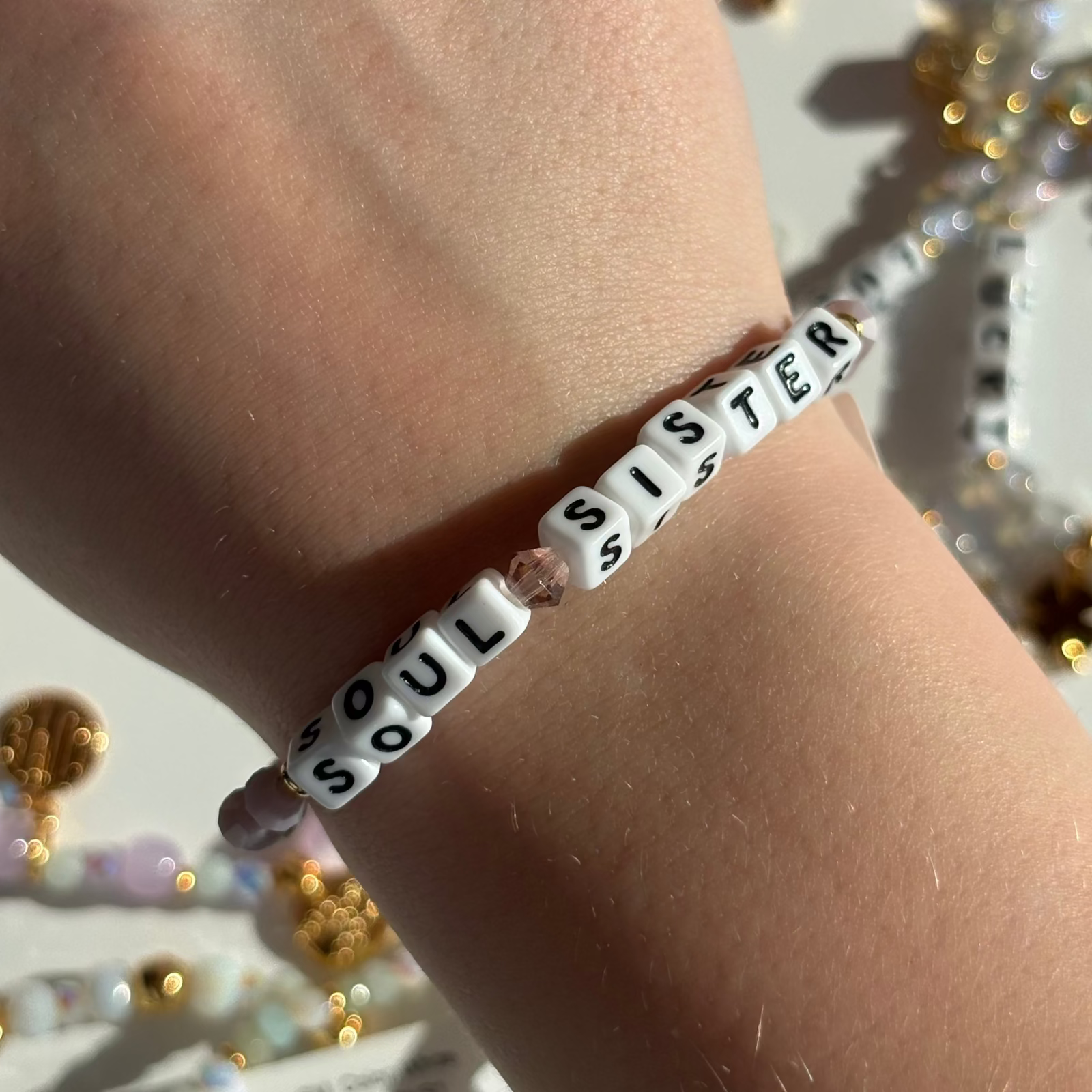 Little Words Project Bracelet with 'Soul Sister' beads on a wrist, with decorative background