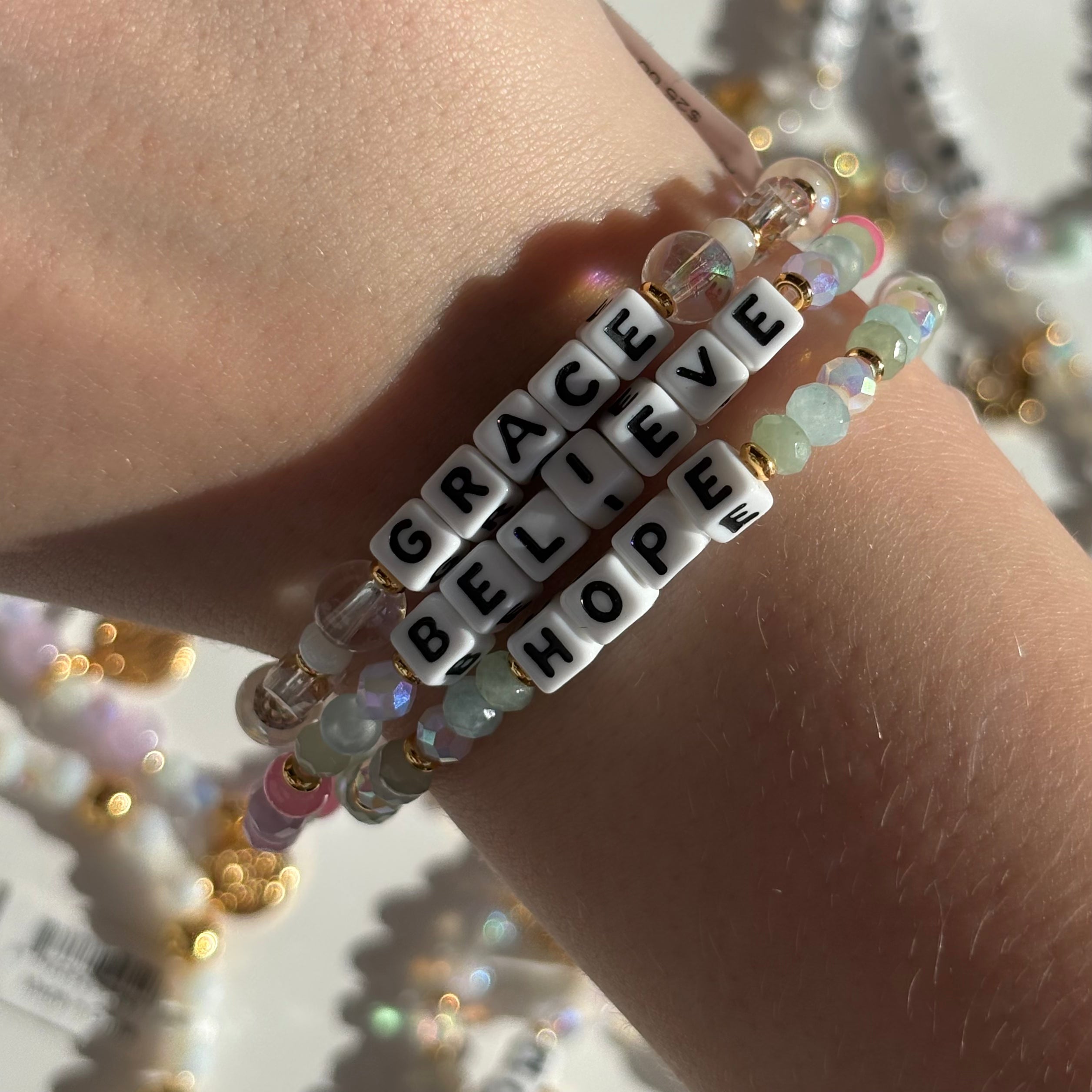 Bracelet with 'GRACE BELIEVE HOPE' beads on a wrist against a blurred background
