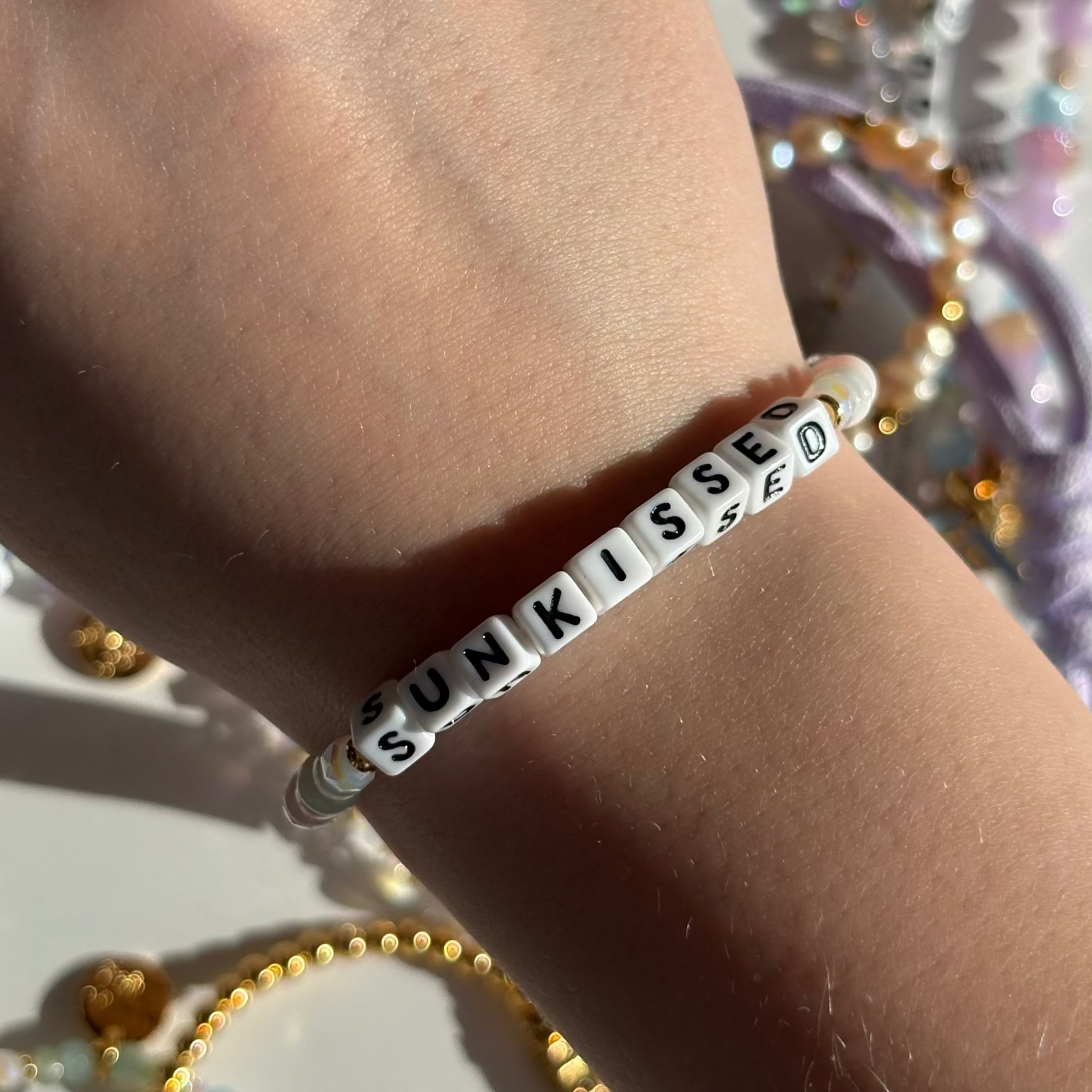 Little Words Project Bracelet with 'SUNKISSED' beads on a wrist against a blurred background