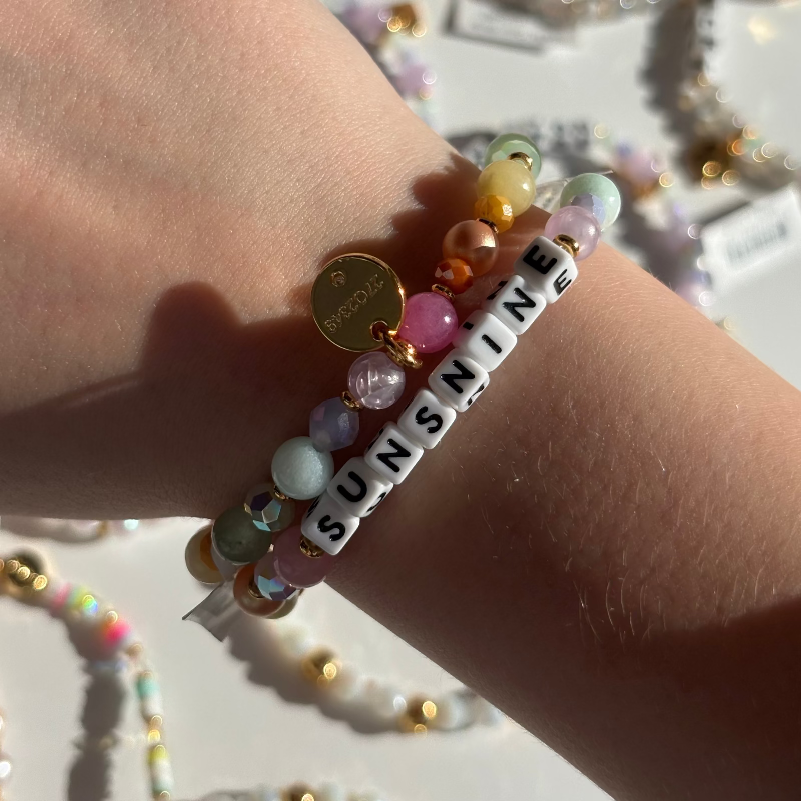 Colorful beaded Little Words Project bracelet with 'SUNSHINE' on a wrist against a blurred background