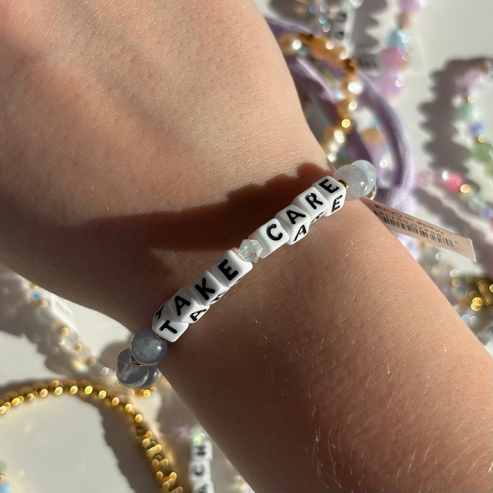 Little Words Project Bracelet with 'Take Care' beads on a wrist against a blurred background