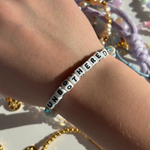 Little Words ProjectBracelet with 'UNBOTHERED' on a wrist with colorful beads in the background