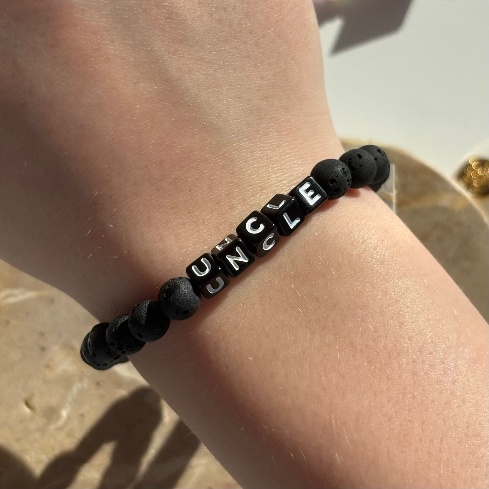Black beaded Little Words Project bracelet with 'UNCLE' on a wrist against a neutral background