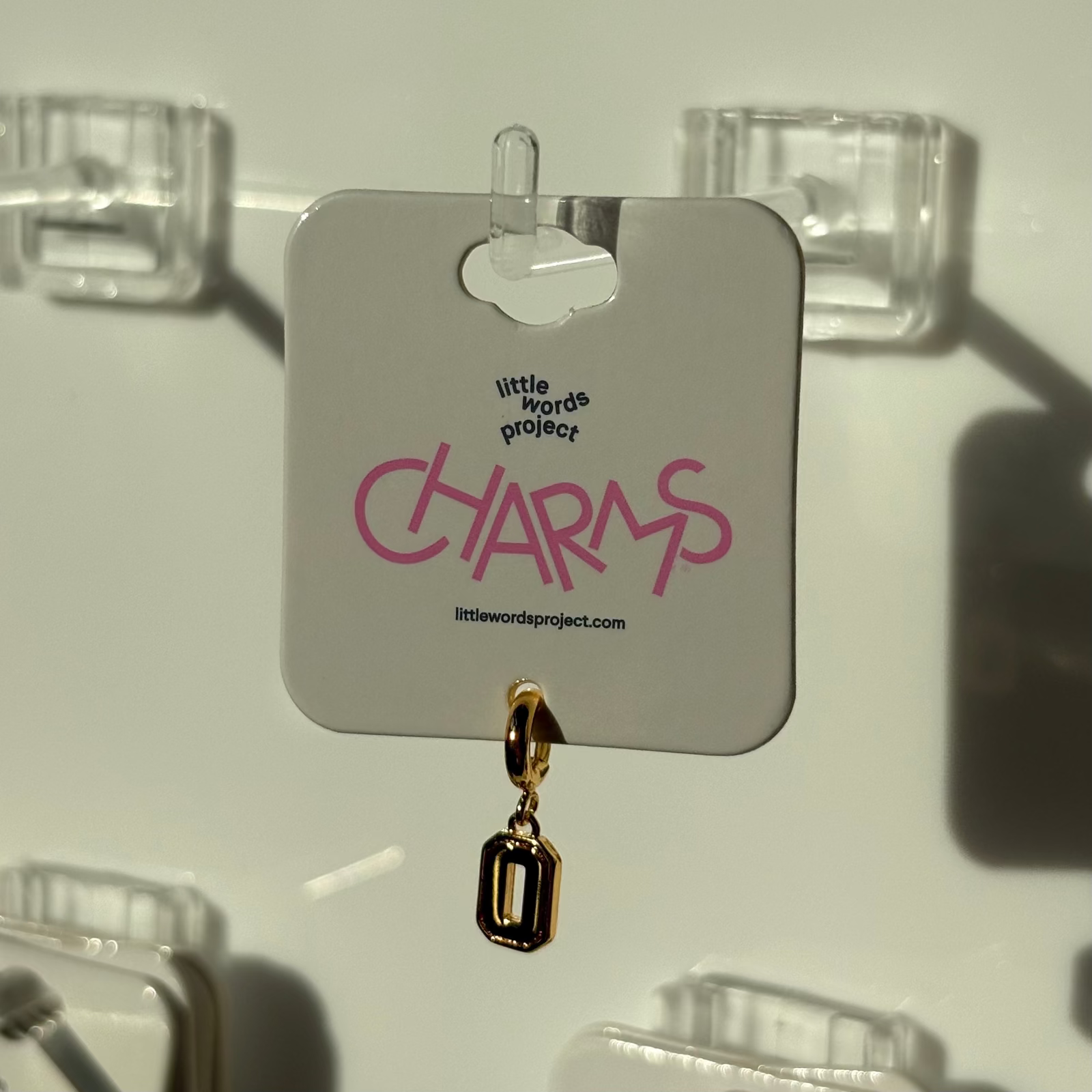 Gold number 0 charm on a 'little words project' card with clear hooks in the background
