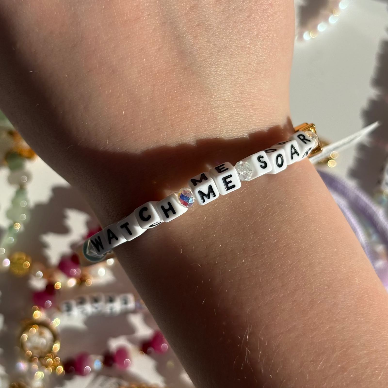 Little Words Project Bracelet with 'Watch Me Soar' on a wrist against a festive background