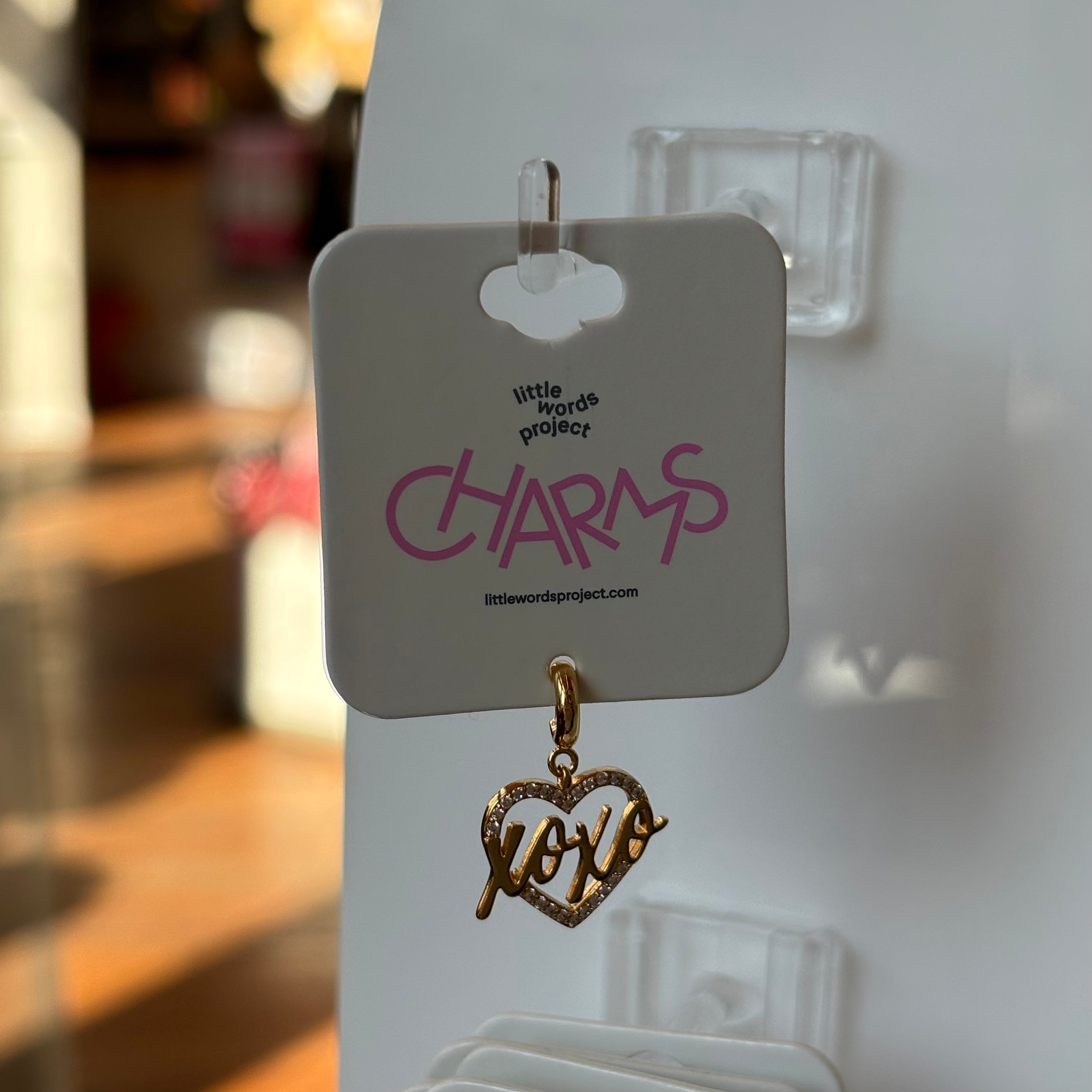 Gold 'xoxo' heart charm on a 'little words project' card with a blurred background.
