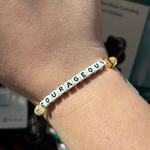 Bracelet with 'COURAGEOUS' beads on a wrist, blurred background