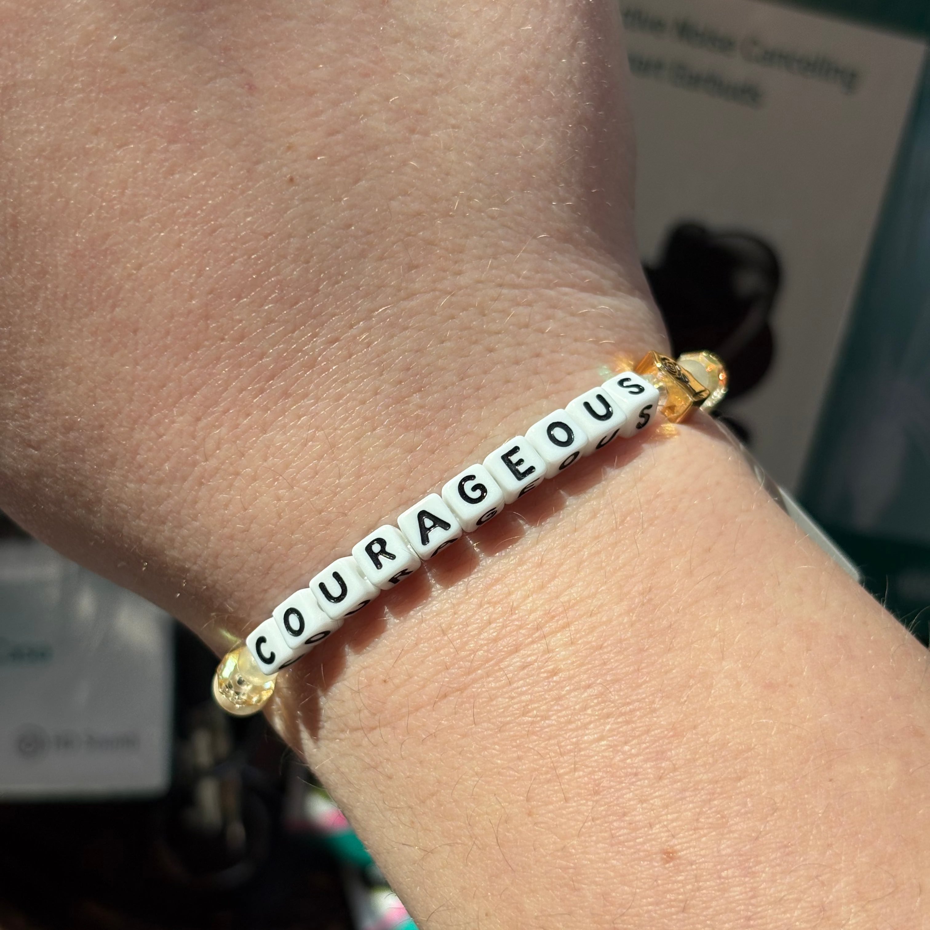 Bracelet with 'COURAGEOUS' beads on a wrist, blurred background