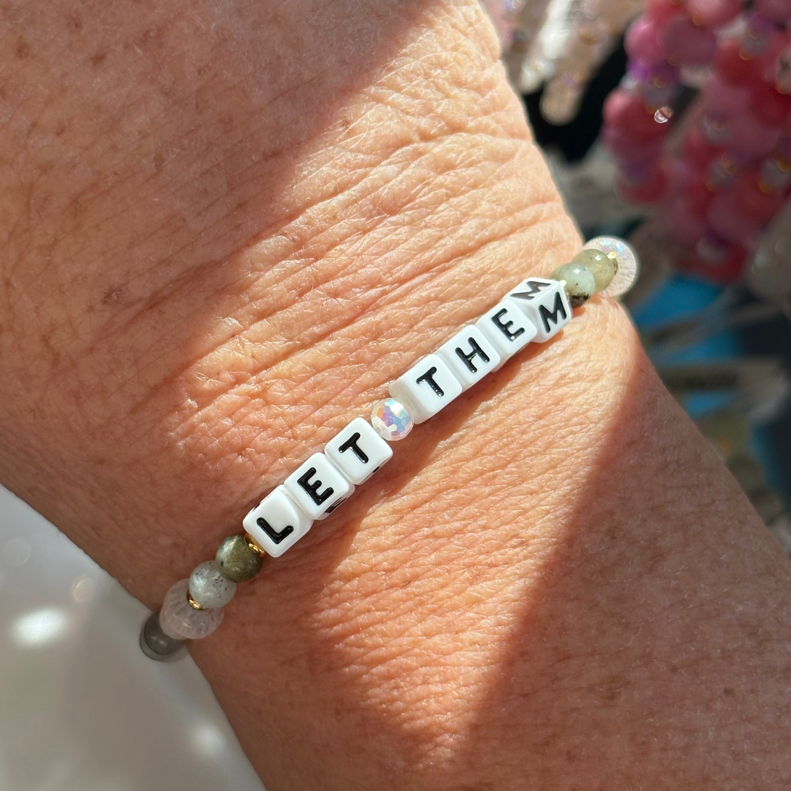 Bracelet with 'LET THEM' beads on a wrist with a blurred background