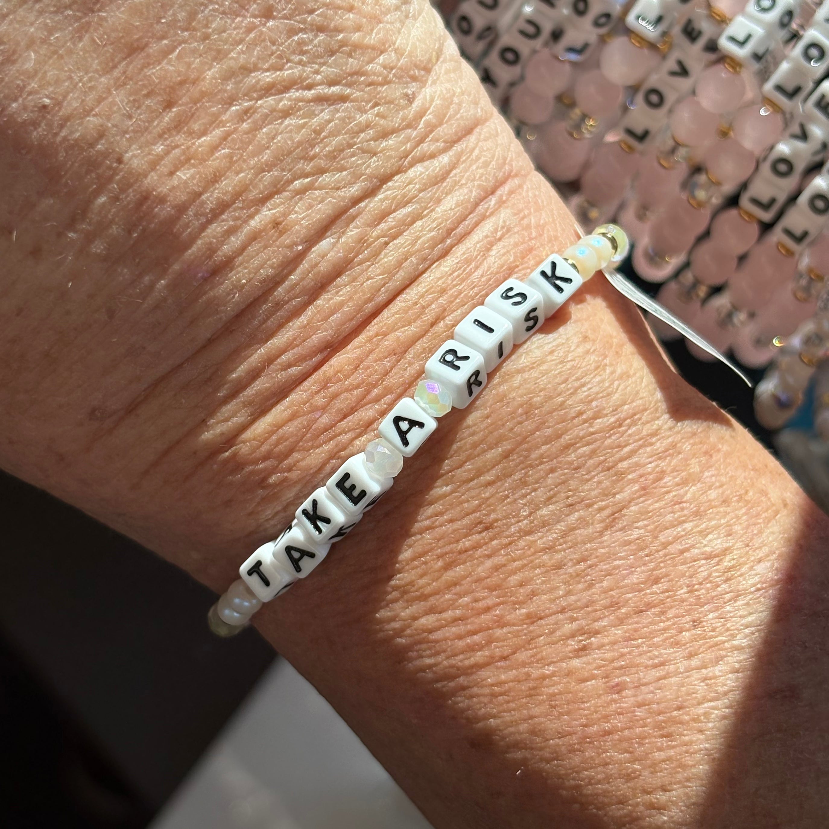 LWP bracelet with 'Take A Risk' beads on a wrist, with a decorative background.