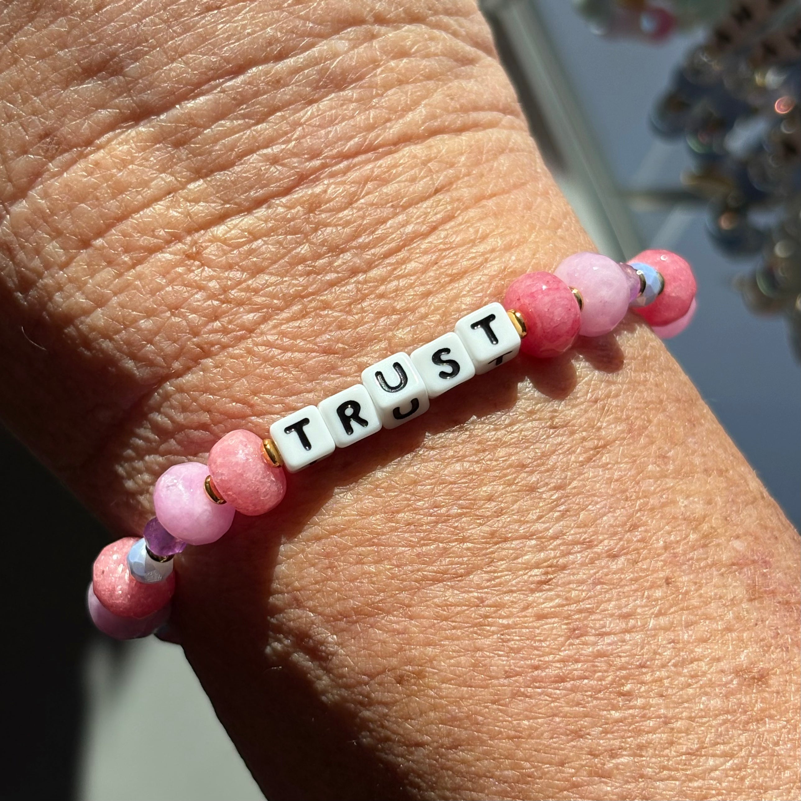 LWP bracelet with pink beads and a white tile spelling 'TRUST' on a wrist.