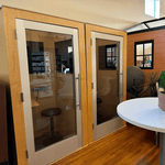 Small sound booths with wooden walls, glass doors, and a white table with a plant.