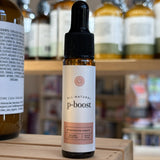 Bottle of Rowe Cosa p-boost supplement with a dropper on a wooden surface, surrounded by other bottles.