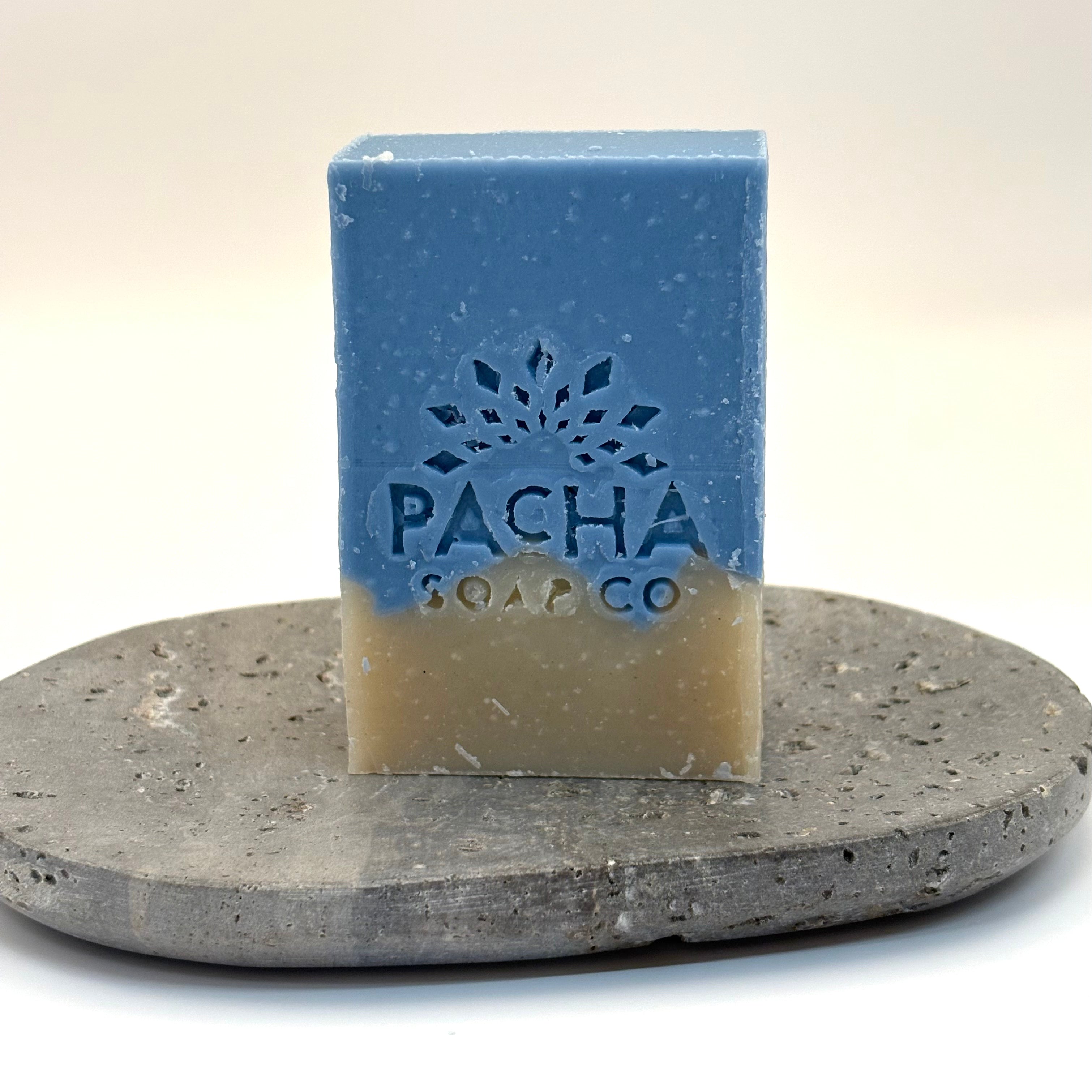 Blue and beige sand and sea soap bar with 'Pacha Soap Co' branding on a stone surface.