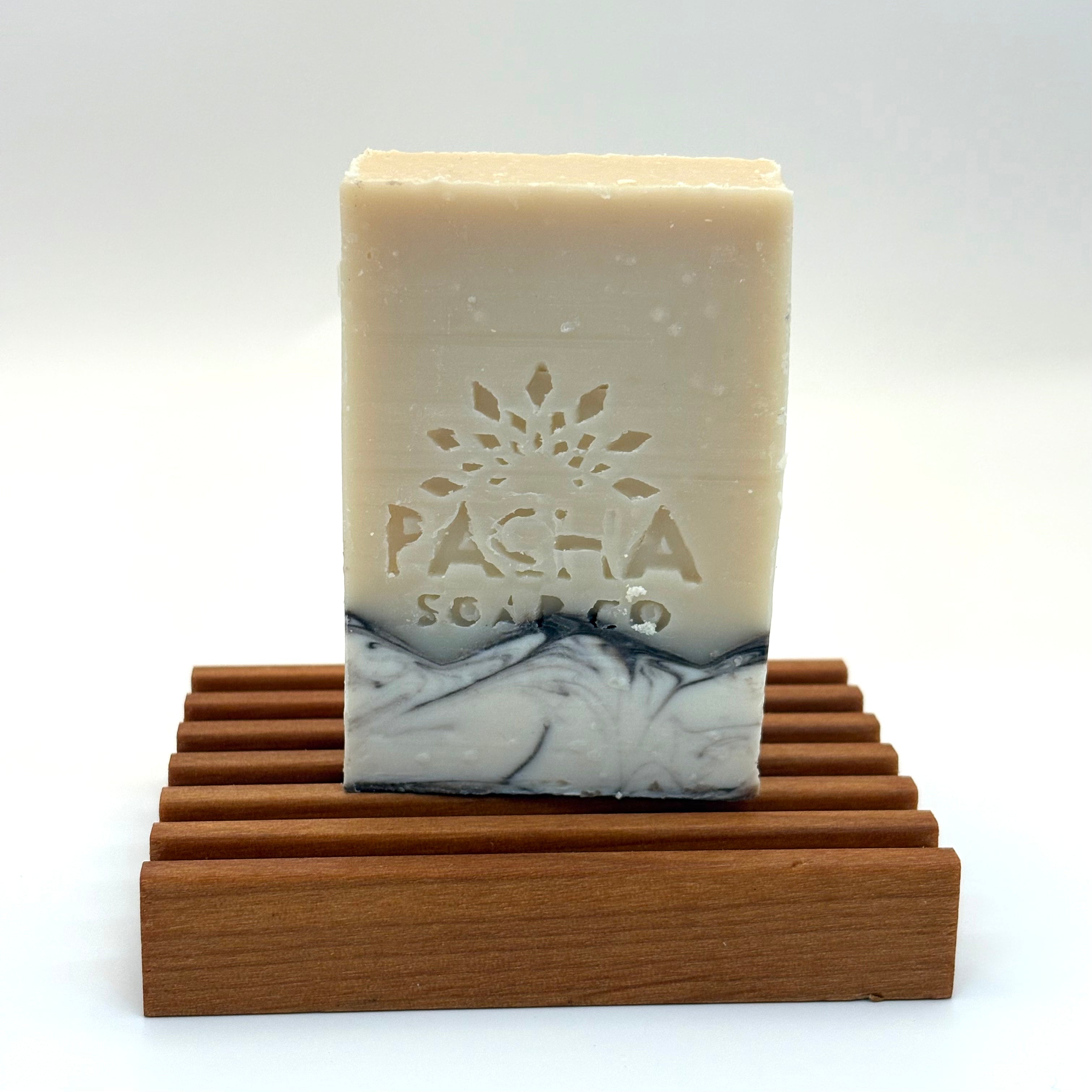 Bar of santal and amber soap with 'Pacha Soap Co' branding on a wooden stand against a white background