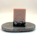 Bar of white blossom and fig soap with Pacha Soap Co logo on a gray stone stand against a white background