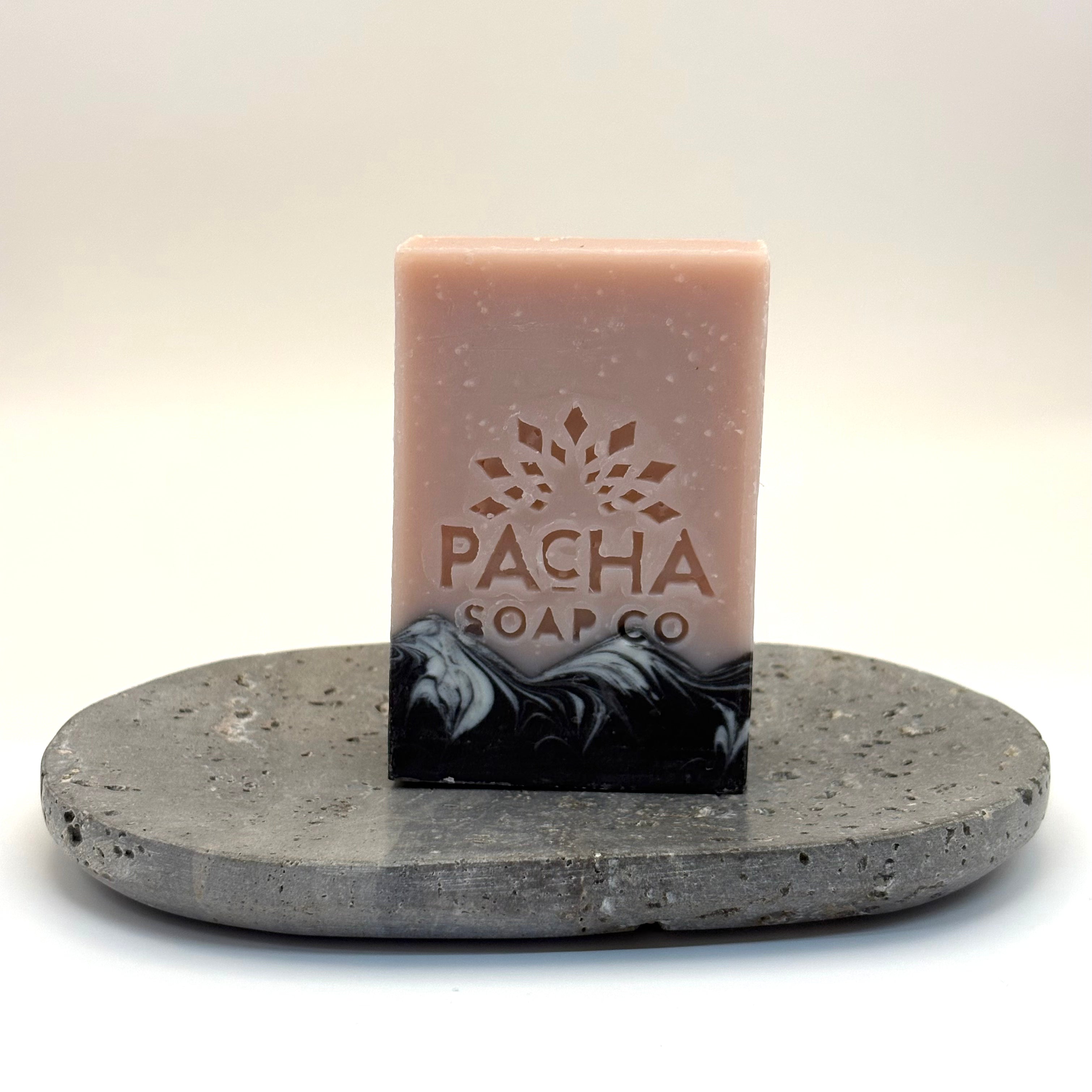 Bar of white blossom and fig soap with Pacha Soap Co logo on a gray stone stand against a white background