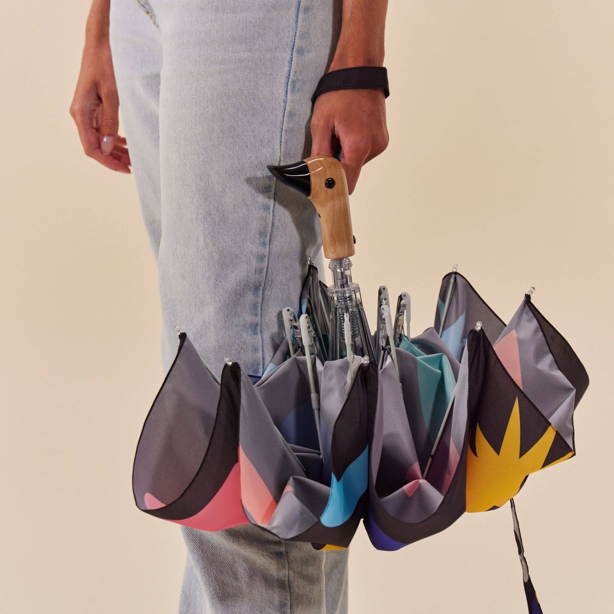 Person holding a unique umbrella with multiple open sections against a beige background