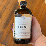 Rowe Casa hand holding a bottle labeled 'Adrenal Support' against a wooden background