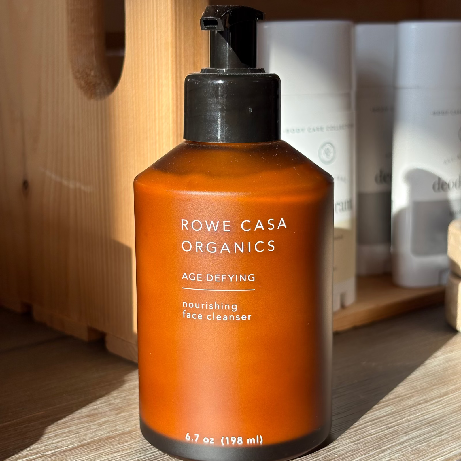 Orange bottle of Rowe Casa Organics face cleanser on a wooden surface