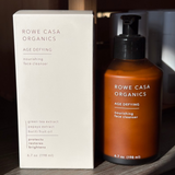 Rowe Casa Organics Age Defying nourishing face cleanser bottle and packaging on a wooden surface.