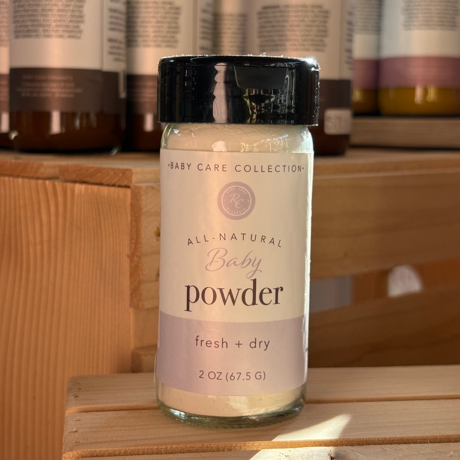 Rowe Casa all-natural baby powder bottle on a wooden surface with other similar bottles in the background.