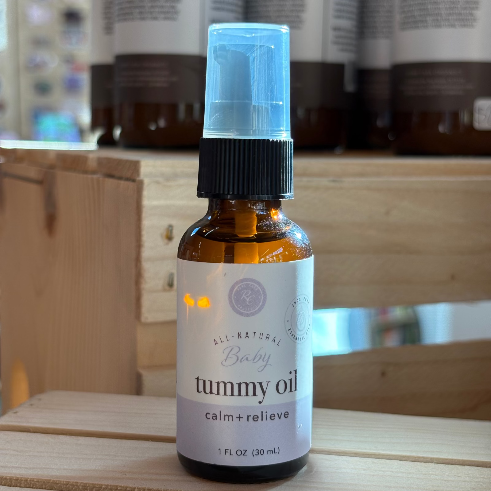 Rowe Casa bottle of baby tummy oil on a wooden surface with blurred bottles in the background