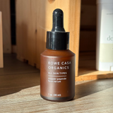 Brown skincare serum bottle with dropper labeled 'Rowe Casa Organics' on a wooden surface.