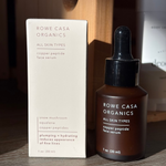 Brown serum bottle with dropper and white box packaging for Rowe Casa Organics on a wooden surface.