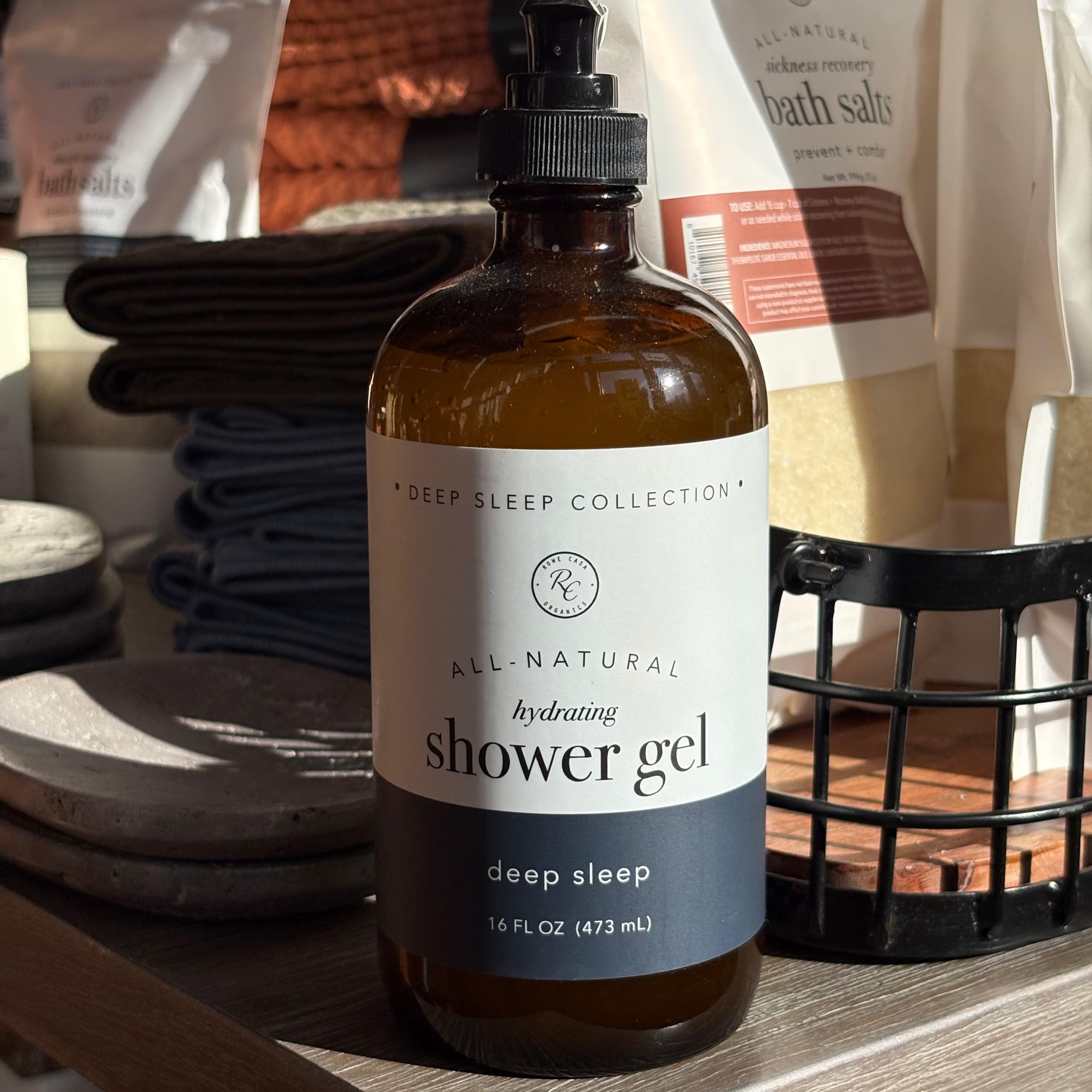 Bottle of all-natural shower gel on a wooden shelf with bath salts in the background.