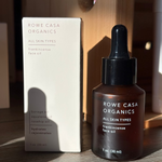 Brown dropper bottle and white box of Rowe Casa Organics Frankincense Face Oil on a wooden surface.