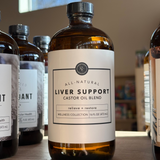 Bottle of 'All-Natural Liver Support' castor oil blend on a wooden surface with other similar bottles in the background.